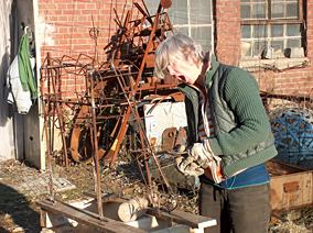 Die Künstlerin vor ihrem Atelier, gähnend mit Eisen arbeitend