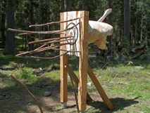 Skulptur aus roh behauenem Holz, Zielscheibe, eingesteckte Äste, halbes Schwein