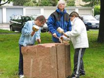 2 Kinder und Gudrun Schuster bearbeiten einen Sandstein
